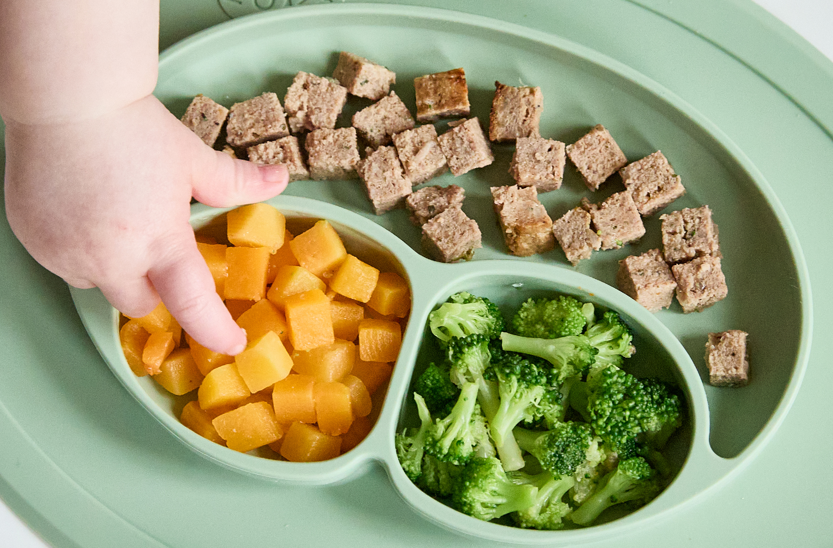 A baby grabbing a piece of Finger Food, using the Nurture Life x ezpz collab. Self-Feeding Starter Pack